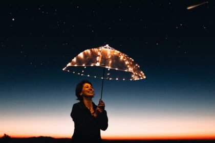 Osoba stoji vani u sumrak, smiješi se i drži prozirni kišobran ukrašen lampicama. Nebo je tamno s vidljivim zvijezdama, a u gornjem desnom kutu vidi se zvijezda padalica. Horizont sjaji od sve slabije sunčeve svjetlosti.