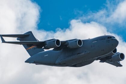 Veliki sivi vojni teretni zrakoplov s četiri motora leti kroz djelomično oblačno plavo nebo. Na boku zrakoplova vidljivi su natpisi "AIR FORCE" i broj "4035", a stajni trap mu je uvučen.